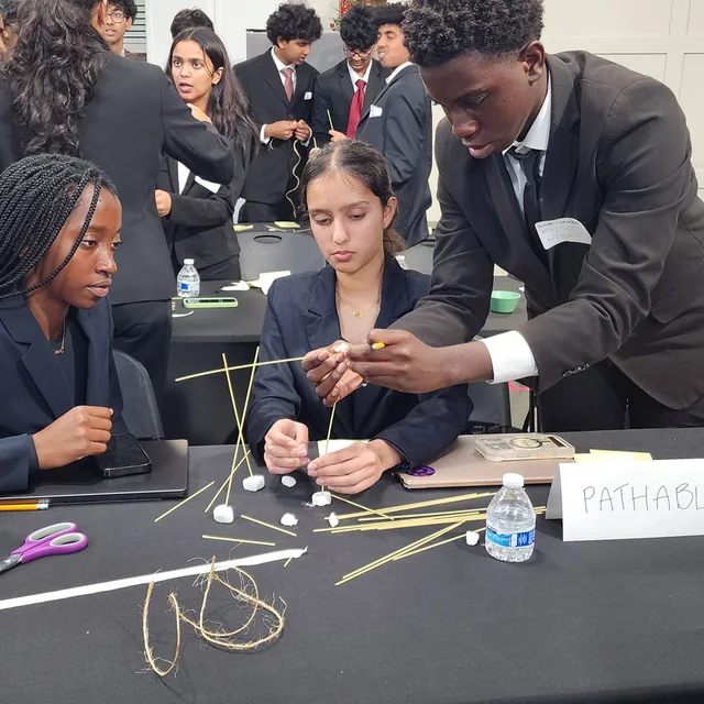 A SharkMakers team building a prototype from spaghetti and tape at a workshop table.