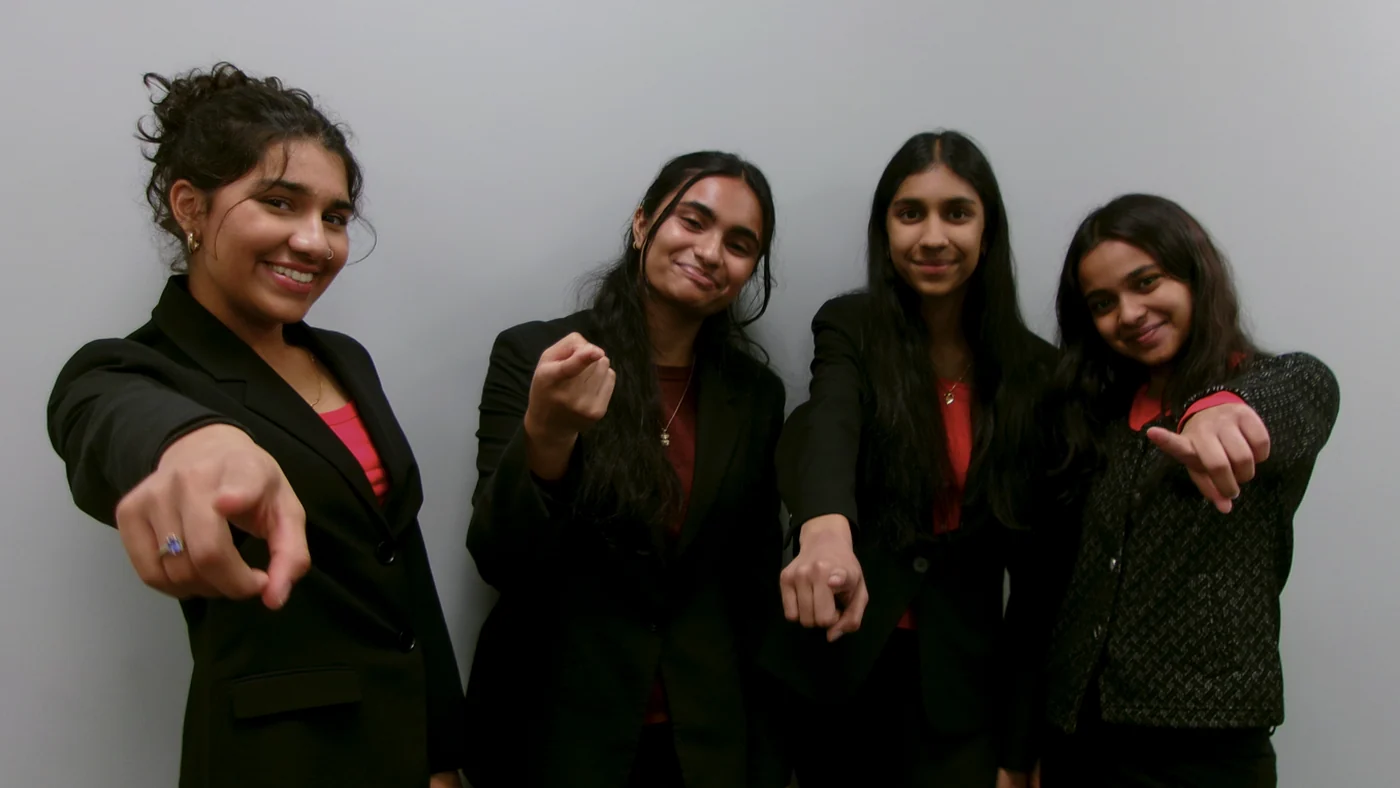 Four SharkMakers students in suits, smiling and pointing at the camera.