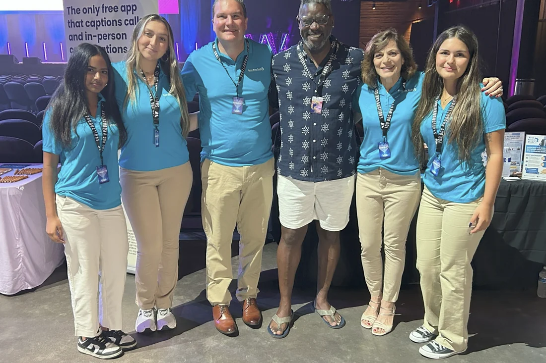 Six people in Connect-IT 360 polo shirts standing with a guest in
                front of an accessibility technology exhibit at the WAWABILITY event.