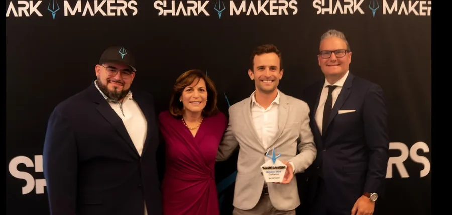 Four industry partners with an award on stage in front of a SharkMakers backdrop.